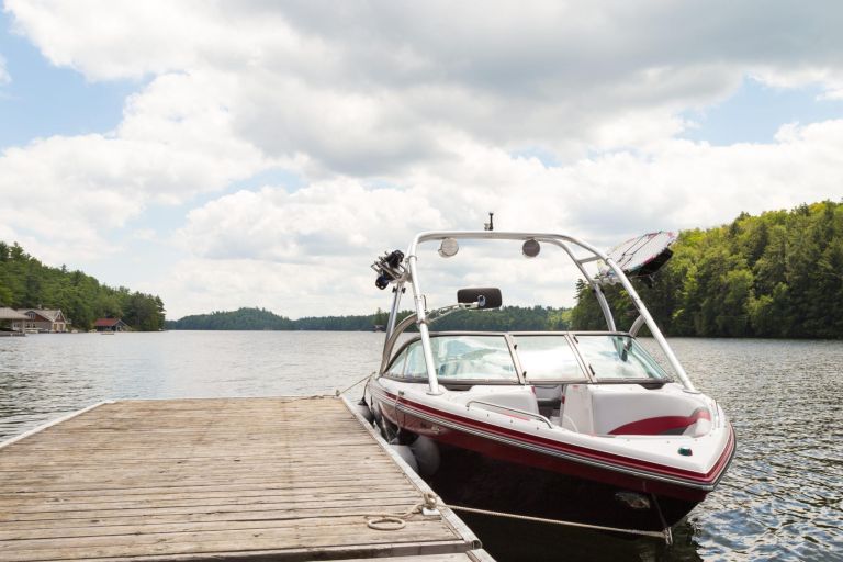 A wakeboard boat at a wooden dock in the Muskokas on a sunny day