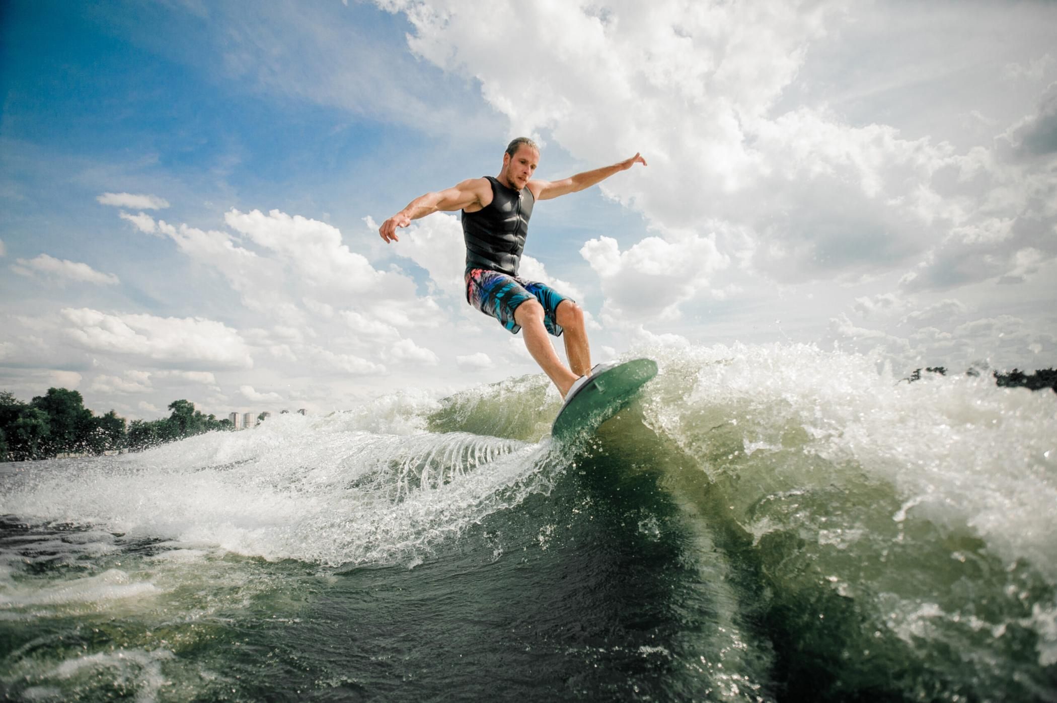 Young and active man wakesurfing on the board down the river against the background of sky